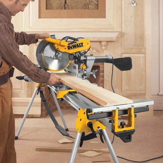 12 inch double bevel sliding compound miter saw being used to cut a long sheet of wood by a worker.